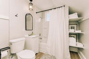 A modern bathroom with a toilet, sink, and shower. There is a towel rack with towels and a framed picture on the wall.