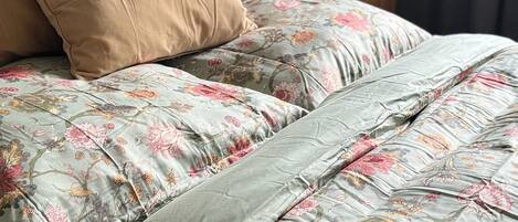 Een net opgemaakt bed met bloemenbeddengoed en een grijze hoofdeinde.