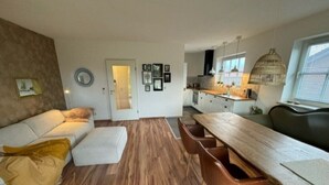 En moderne stue med sofa, skammel og et spiseområde med et træbord og stole.