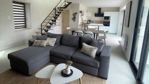 Un salon moderne comprenant un canapé d’angle, un coin repas et un escalier menant à un autre niveau.