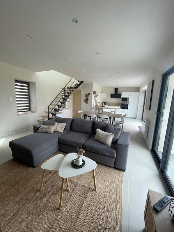A modern living room with a sectional sofa, a dining area, and a staircase leading to another level.