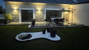 Une maison en pierre dotée d’un patio, d’un espace extérieur aménagé pour s’asseoir et d’un jardin bien éclairé.