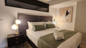 Een net opgemaakt bed met een groene deken en witte kussens, een bedlampje en een wanddecoratie.