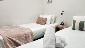 A hotel room with two beds, each with a pillow and a blanket. There is a nightstand with a lamp between the beds. - Collins St - The Heart Of The City (Melbourne)