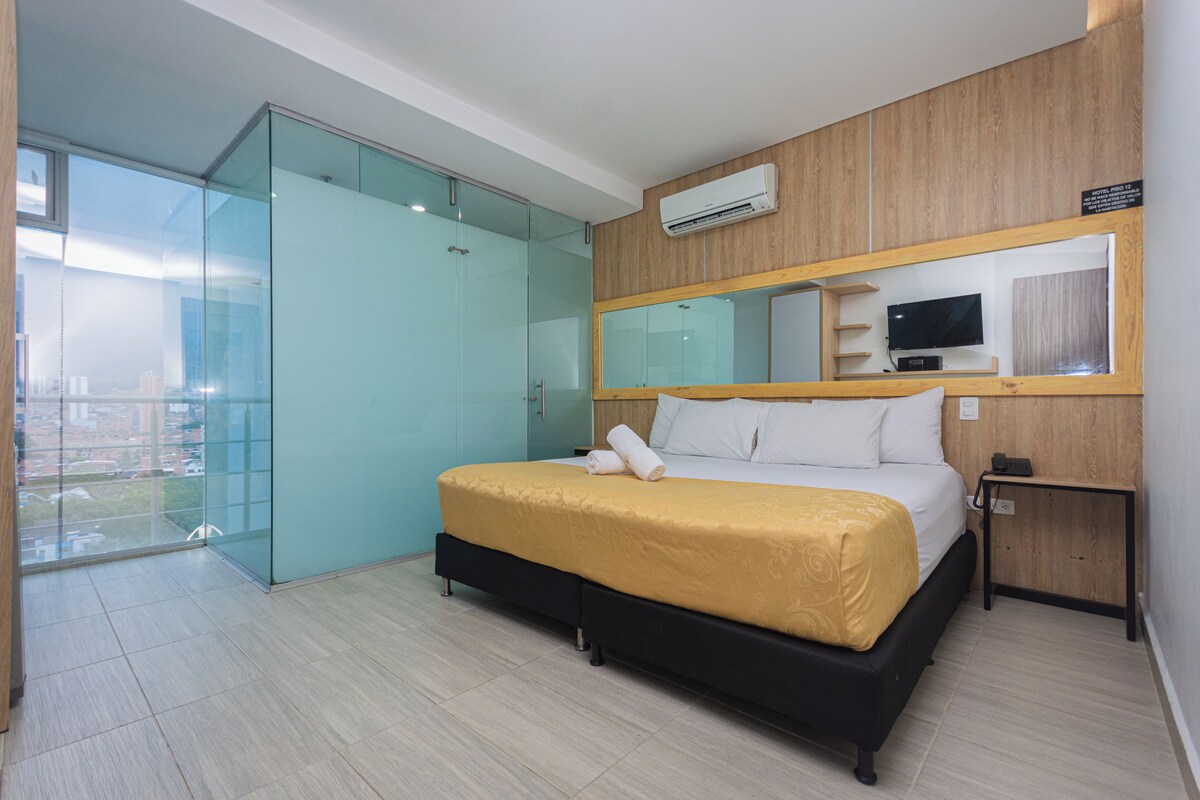 A hotel room with a bed, a television, a mirror, and a sliding glass door leading to a balcony.