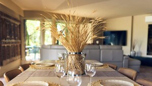 Una mesa de comedor dispuesta con platos, copas de vino y un florero con espigas de trigo.