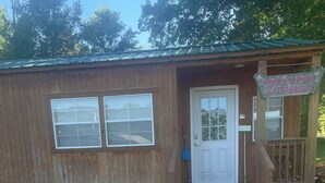 A wooden cabin with a white door, a porch, and a sign that reads "Welcome to Breakfast." - Tiny Cozy Home in Missouri (Bakersfield)