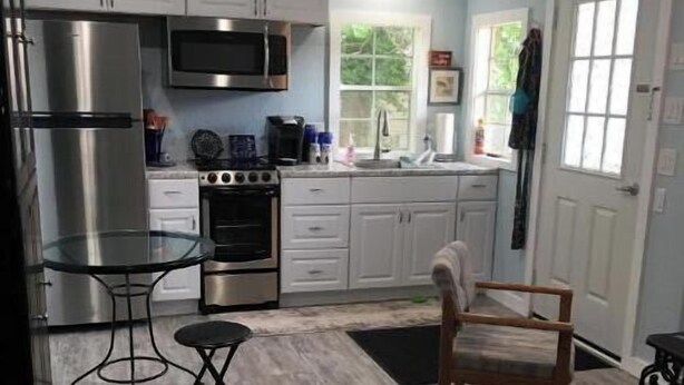 A kitchen with white cabinets, stainless steel appliances, a glass table, and a wooden chair. - Tiny Cozy Home in Missouri (Bakersfield)