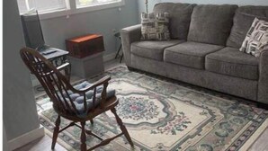 A living room with a gray sofa, a patterned rug, a wooden chair, and a ceiling fan. - Tiny Cozy Home in Missouri (Bakersfield)