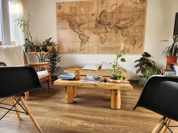 Een gezellige kamer met een houten bijzettafeltje, boeken, een kaart aan de muur en diverse kamerplanten.