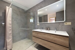 Ein modernes Badezimmer mit Dusche, einem großen Spiegel und einem Waschtisch.