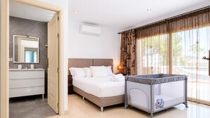 Ein Hotelzimmer mit einem Bett, einem Nachttisch, einer Lampe, einem Reisebett und einem großen Fenster mit Vorhängen.