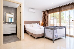 Ein Hotelzimmer mit einem Bett, einem Nachttisch, einer Lampe, einem Reisebett und einem großen Fenster mit Vorhängen.