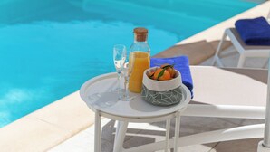 Ein Tisch am Pool mit einer Flasche, Gläsern und einer Obstschale.