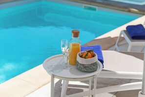 Ein Tisch am Pool mit einer Flasche, Gläsern und einer Obstschale.