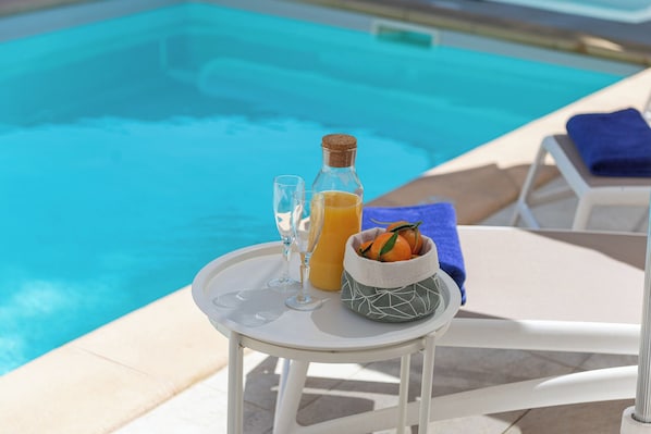 Ein Tisch am Pool mit einer Flasche, Gläsern und einer Obstschale.