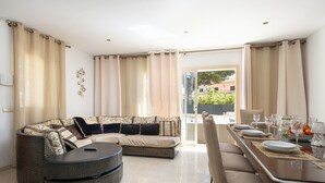 Ein modernes Wohnzimmer mit einem Ecksofa, einem runden Couchtisch und einem Essbereich mit Tisch für vier Personen.