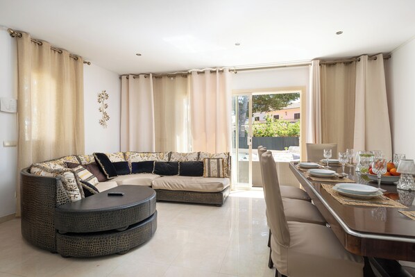 Una sala de estar moderna con un sofá modular, una mesa de centro redonda y un comedor con una mesa preparada para cuatro.
