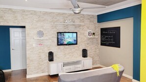 A modern living room with a stone wall, a flat-screen TV, a ceiling fan, and a chalkboard with Wi-Fi details. - Spacious full equipped in quiet area w/terrace B (Willemstad)