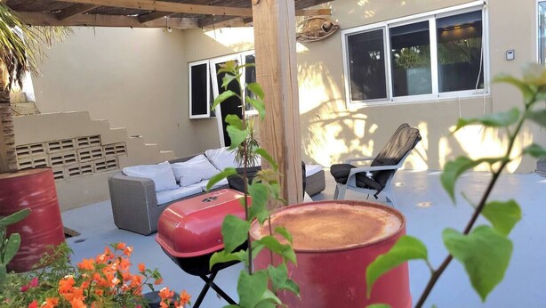 A covered outdoor seating area with a grill, cushions, and a window overlooking a garden. - Spacious full equipped in quiet area w/terrace B (Willemstad)