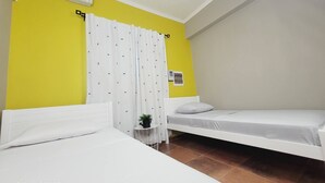 A hotel room with two single beds, a yellow accent wall, white curtains, and an air conditioning unit. - Spacious full equipped in quiet area w/terrace B (Willemstad)