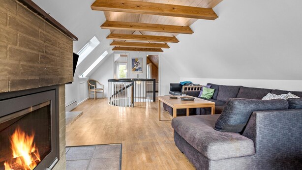 A loft-style living room with a fireplace, wooden beams, a sofa, and a dining table. - Stunning home in Vestervig with sauna (Vestervig)