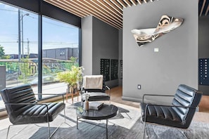 Un hall dâentrĂ©e moderne avec deux fauteuils en cuir, une table en verre, une plante en pot et une grande Ćuvre dâart abstraite accrochĂ©e au mur.