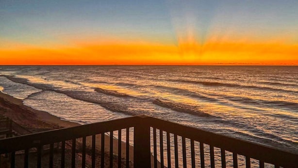 Um pôr do sol sobre o oceano, com ondas refletindo as cores do céu.