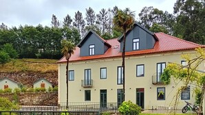 A two-story building with a red-tiled roof, multiple windows, and a stone wall in the background. - Quinta dos Tojais (Celorico de Basto)