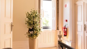 A hallway with a wooden floor, a large potted plant, and a fire extinguisher on the wall. - Quinta dos Tojais (Celorico de Basto)