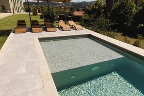 Une piscine avec des chaises longues en bois et une terrasse carrelée.