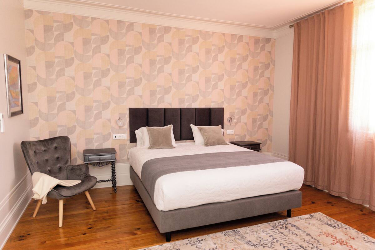 Ein Schlafzimmer mit einem großen Bett, einem Sessel, einem Nachttisch und einer Wand mit Muster.
