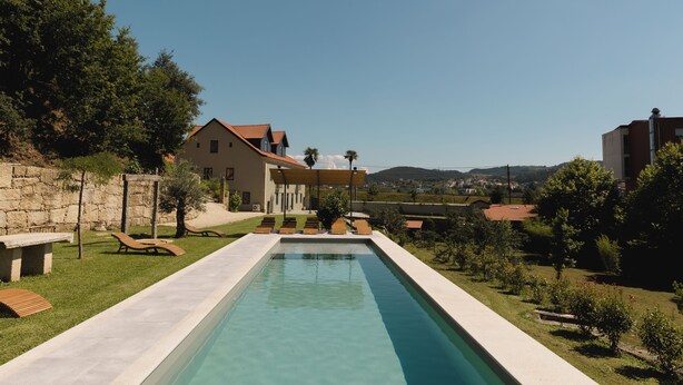 A swimming pool with lounge chairs, a stone wall, and a house in the background. - Quinta dos Tojais (Celorico de Basto)
