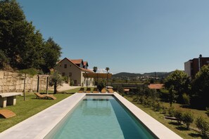 A swimming pool with lounge chairs, a stone wall, and a house in the background. - Quinta dos Tojais (Celorico de Basto)