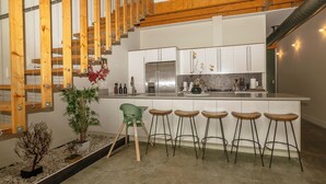 Eine moderne Küche mit einer zentralen Kochinsel, Barhocker und einer Treppe mit Holzbalkon.