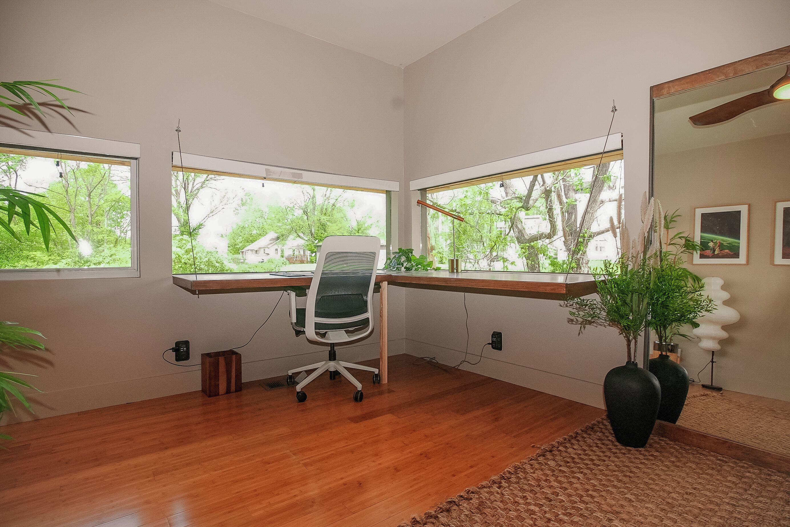 Un espacio de oficina moderno con un escritorio de madera, una silla de oficina y grandes ventanales con vistas a zonas verdes.