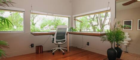 Un espacio de oficina moderno con un escritorio de madera, una silla de oficina y grandes ventanales con vistas a zonas verdes.