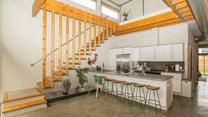 Eine moderne Küche mit einer zentralen Kochinsel, Barhocker und einer Holztreppe.
