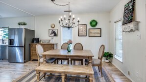 A dining area with a wooden table, chairs, a chandelier, and a refrigerator in the background. - Historic Downtown Frisco- Walk to Dining- 5m to Toyota Stadium- 12m to Universal (Frisco)