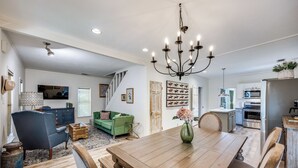 A spacious living room with a large wooden dining table, a green sofa, and a chandelier. - Historic Downtown Frisco- Walk to Dining- 5m to Toyota Stadium- 12m to Universal (Frisco)