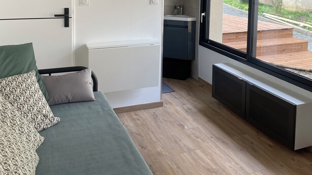 A modern living room with a green sofa, a large window, and a view of the outdoor garden. - Studio Vichy (Vichy)