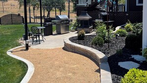 A patio area with outdoor furniture, a barbecue grill, and a stone pathway leading to a house.
