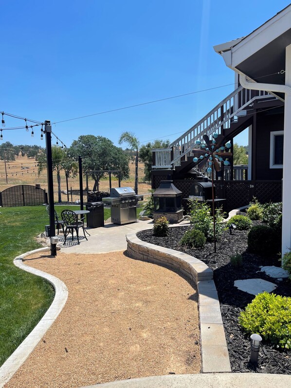 A patio area with outdoor furniture, a barbecue grill, and a stone pathway leading to a house.