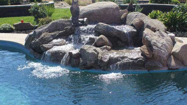 A rock waterfall feature in a landscaped garden with a pool.