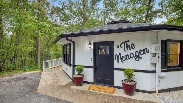 A small, white building with black trim and a black door, labeled "10 The Noragor." There are two potted plants in front, and a welcome mat on the ground. - Fun & Funky Asheville Home with Pool Table, Darts (Arden)