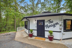 A small, white building with black trim and a black door, labeled "10 The Noragor." There are two potted plants in front, and a welcome mat on the ground. - Fun & Funky Asheville Home with Pool Table, Darts (Arden)