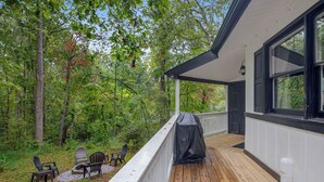 A wooden deck with outdoor seating and a covered grill area, surrounded by trees. - Fun & Funky Asheville Home with Pool Table, Darts (Arden)