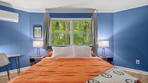 A bedroom with a large bed, two bedside tables with lamps, a window with curtains, and a chair. - Fun & Funky Asheville Home with Pool Table, Darts (Arden)