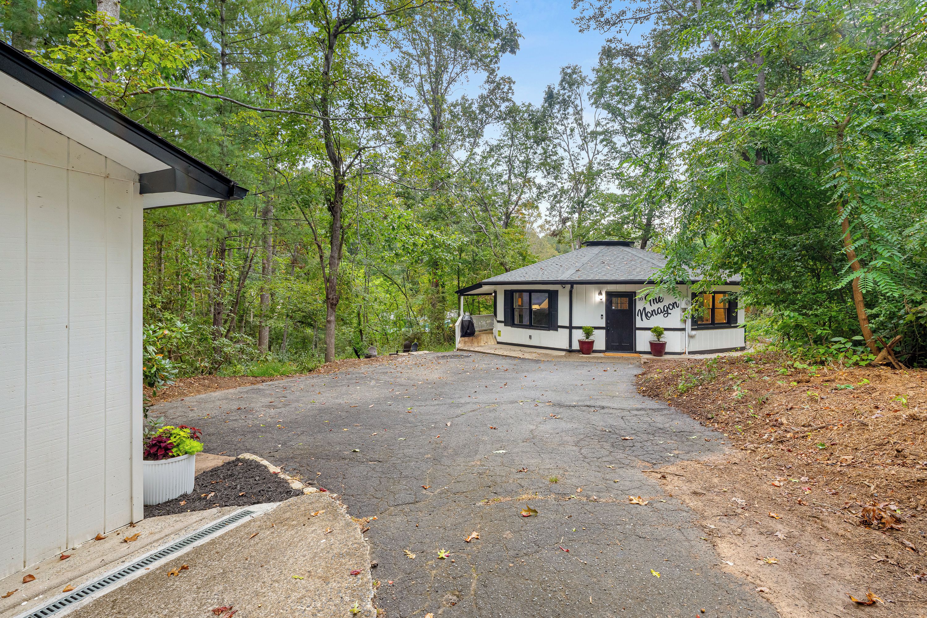 Un chalet isolé, accessible par une allée pavée qui mène à une porte en bois, et entouré d’une forêt dense.