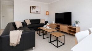 Een moderne woonkamer met een zwarte bank, een houten salontafel, een televisie op een houten dressoir, en een deur op de achtergrond.